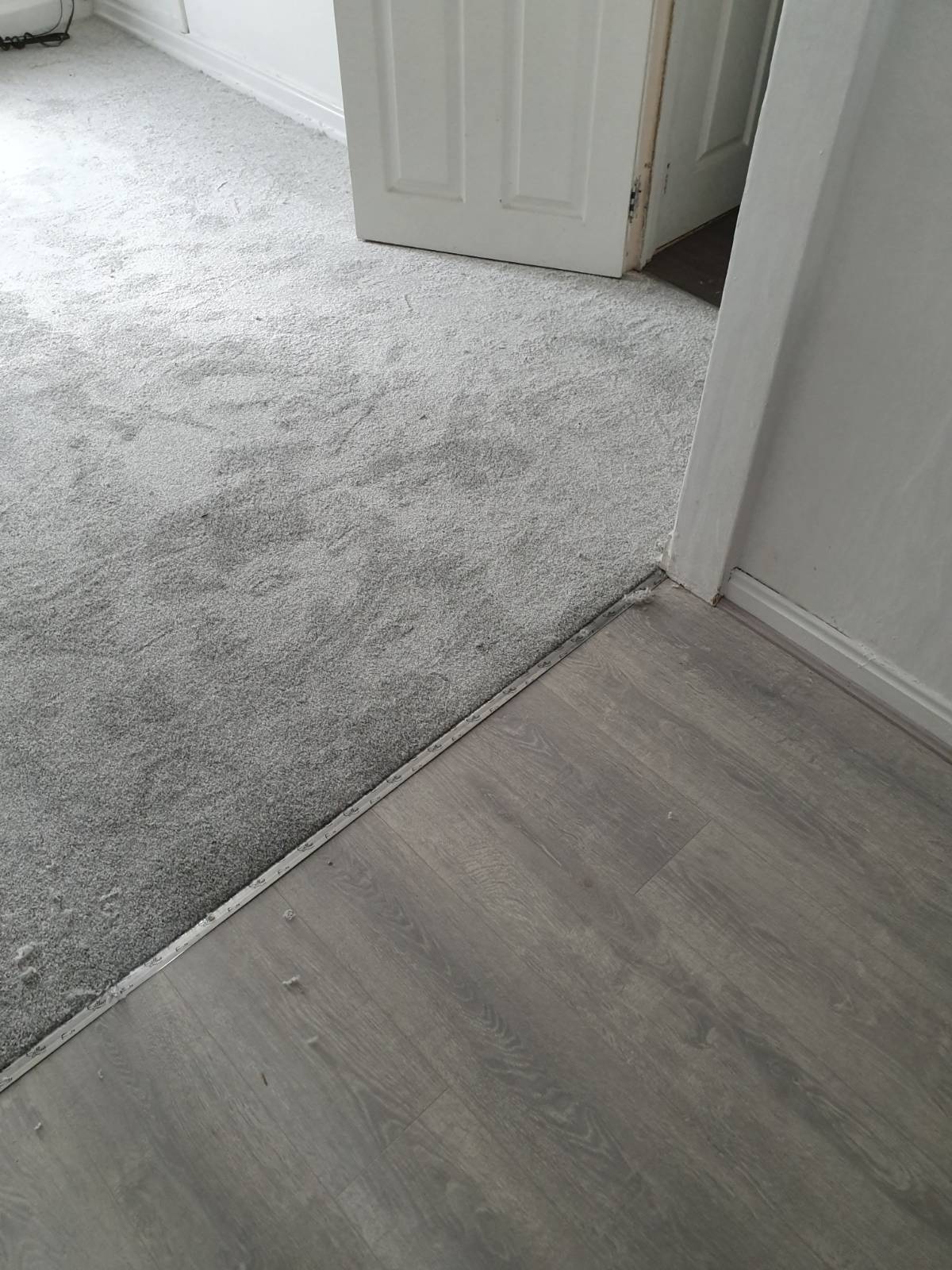 living area split by half grey laminate flooring and half carpet 